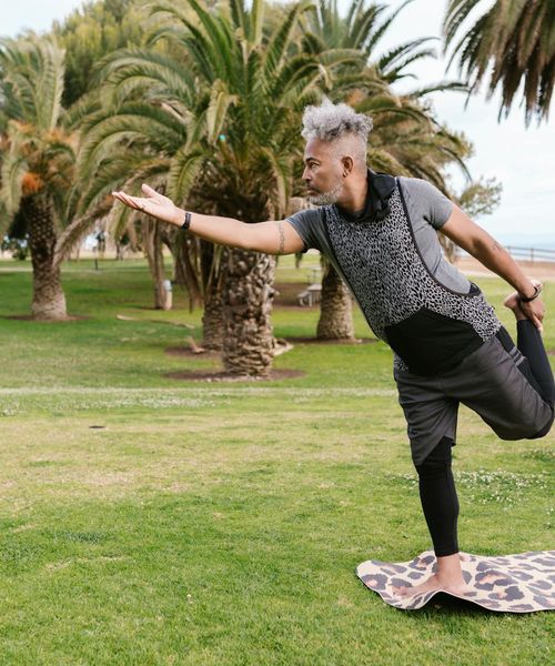Man performing a balancing exercise on one leg in a calm park.